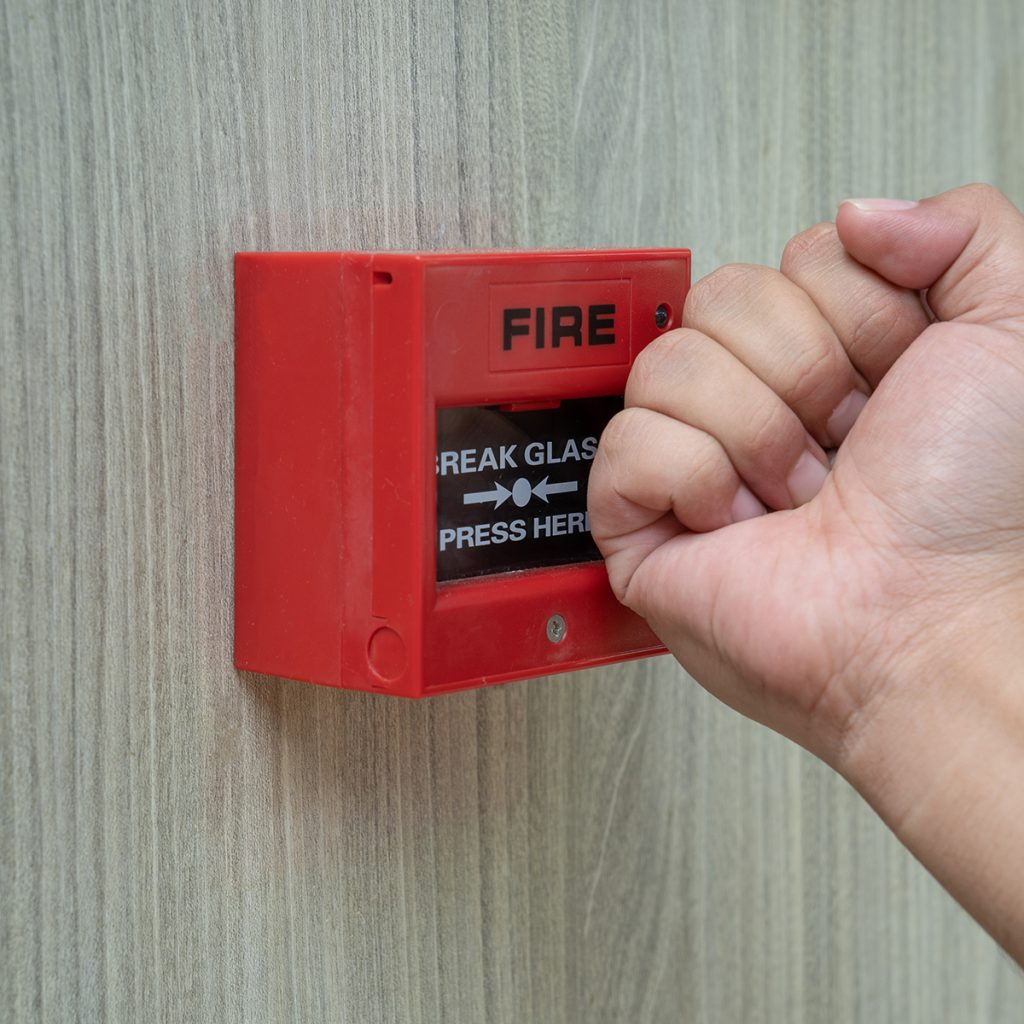 Main appuyant sur un détecteur incendie (boîtier rouge)